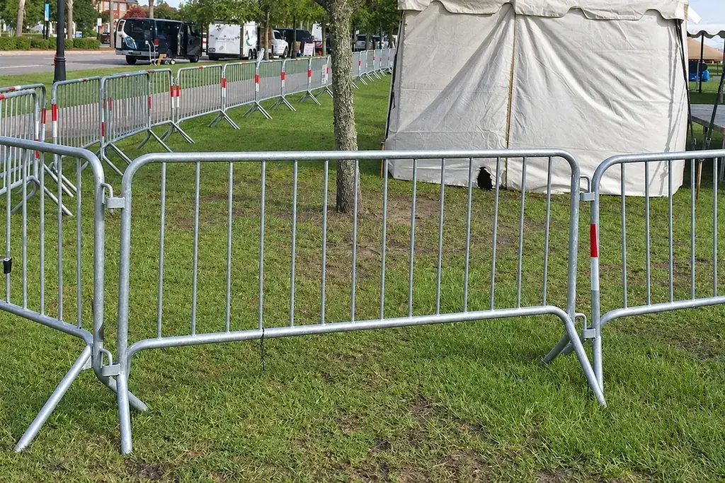 Fixed-leg metal crowd barriers arranged on grass beside an event area