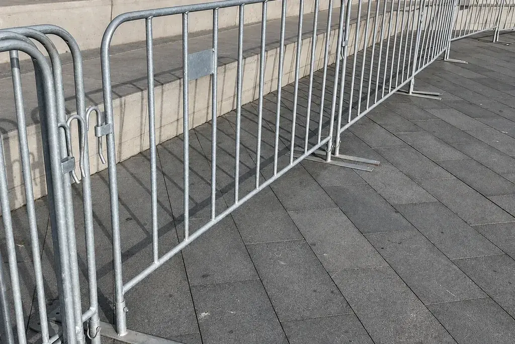 Line of metal crowd barriers with projecting feet along a paved route