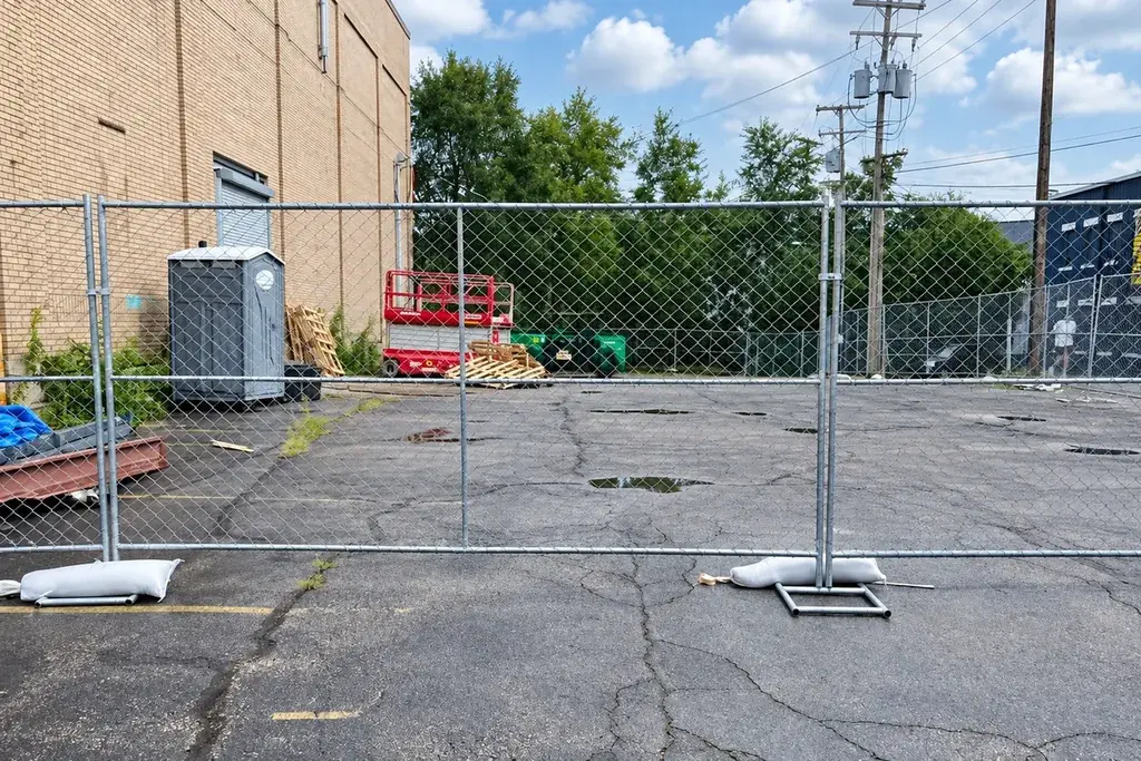 Temporary chain link fence panels and support feet across a paved site
