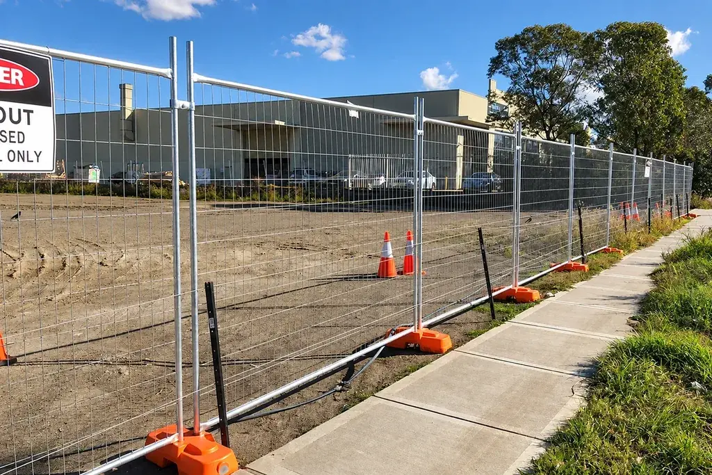 Temporary mesh fence panels with support feet along a paved site