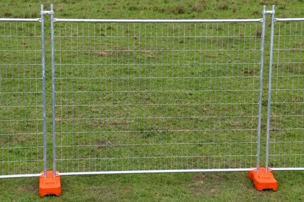 Temporary welded mesh panels joined at posts with orange support feet on grass