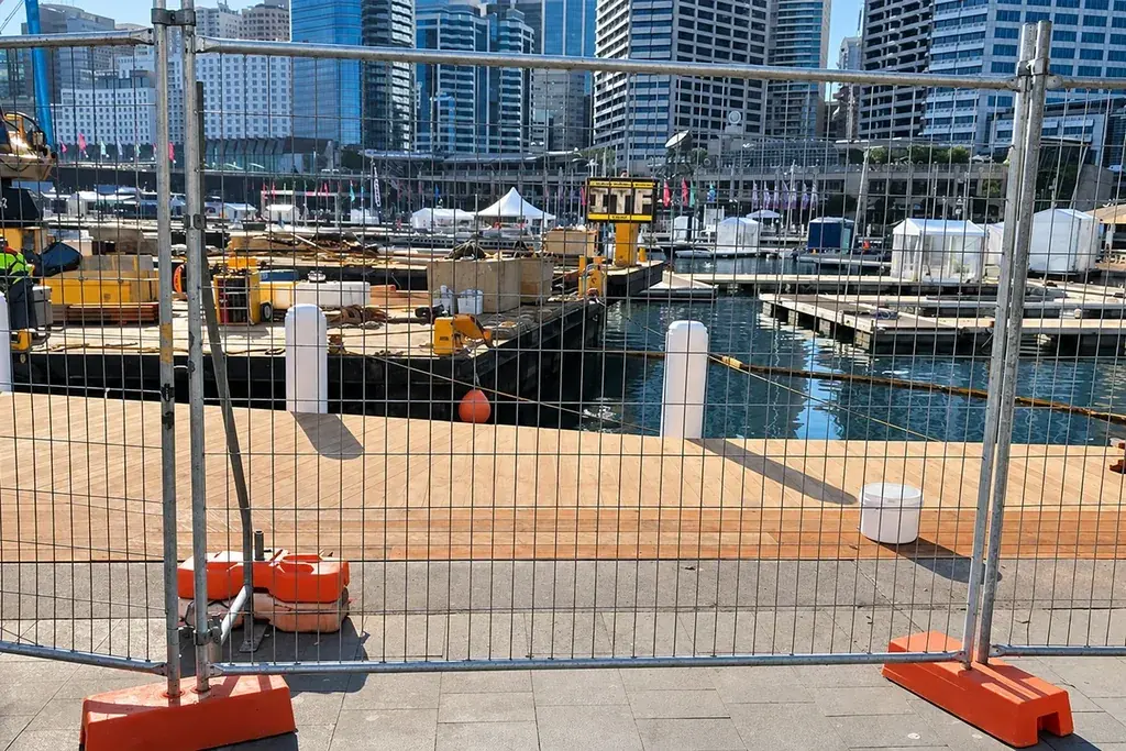 Temporary welded mesh fence and orange support feet beside a waterfront work area