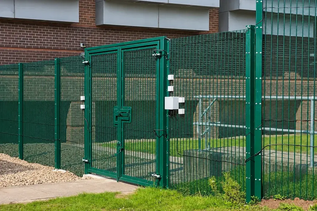 Green coated mesh fence and gate installed beside a utility building