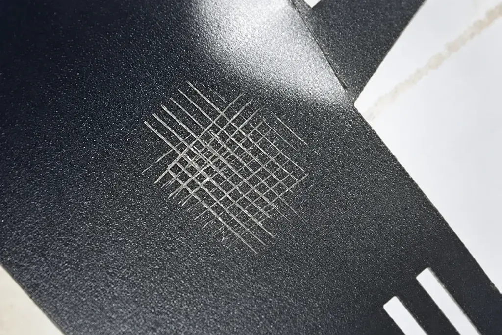 Cross-hatch cut pattern on a dark coated metal sample