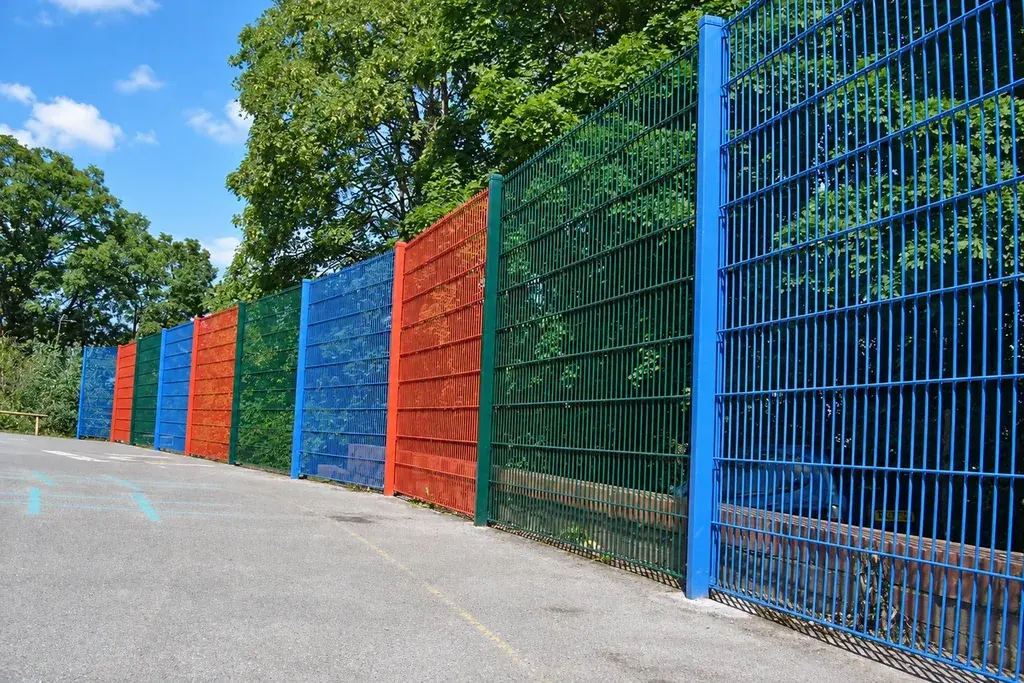 Blue, green and red twin-wire fence panels beside a paved path