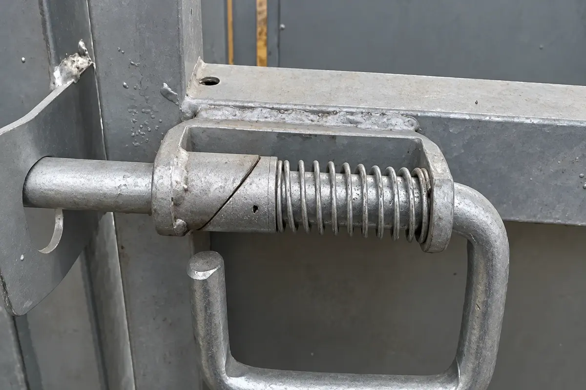 Spring-loaded metal gate latch mounted on a gate frame
