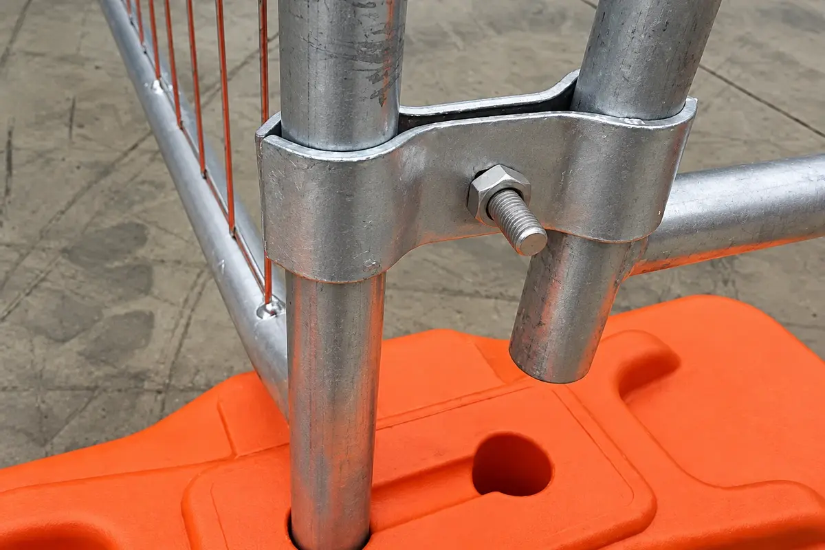 Metal clamp joining temporary fence tubes above an orange foot