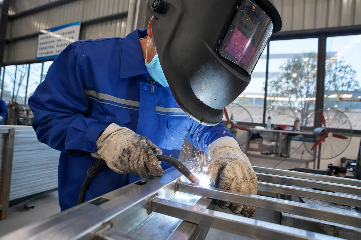 Welder joining steel fence frame sections in a workshop