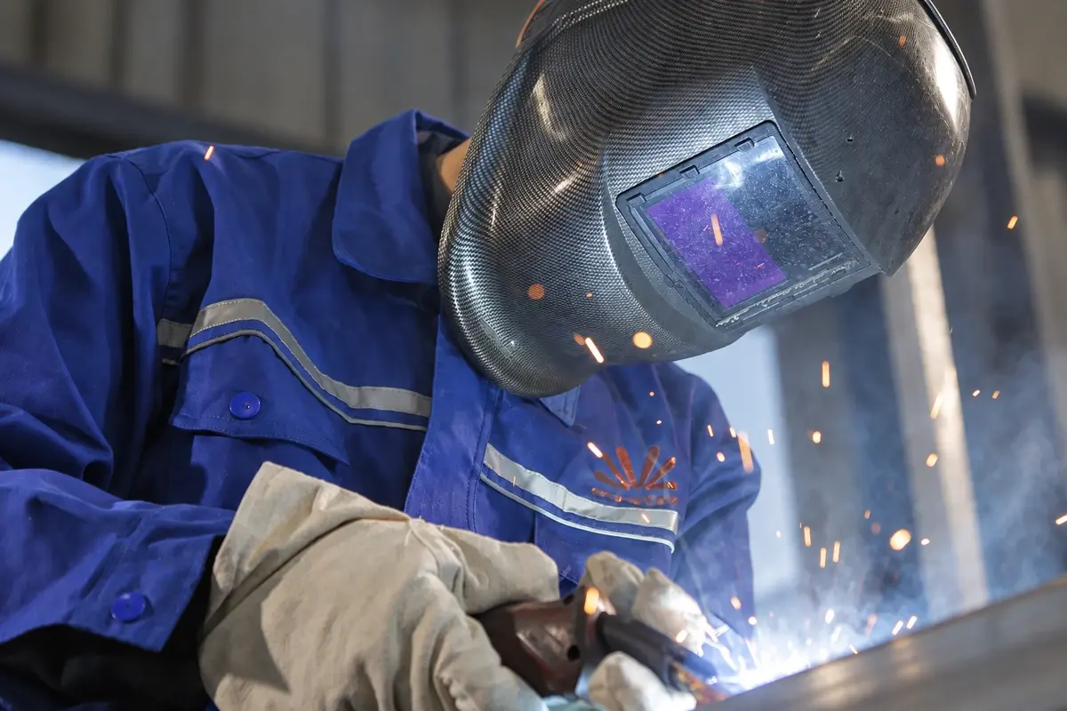 Welder working on a steel fence component in a workshop