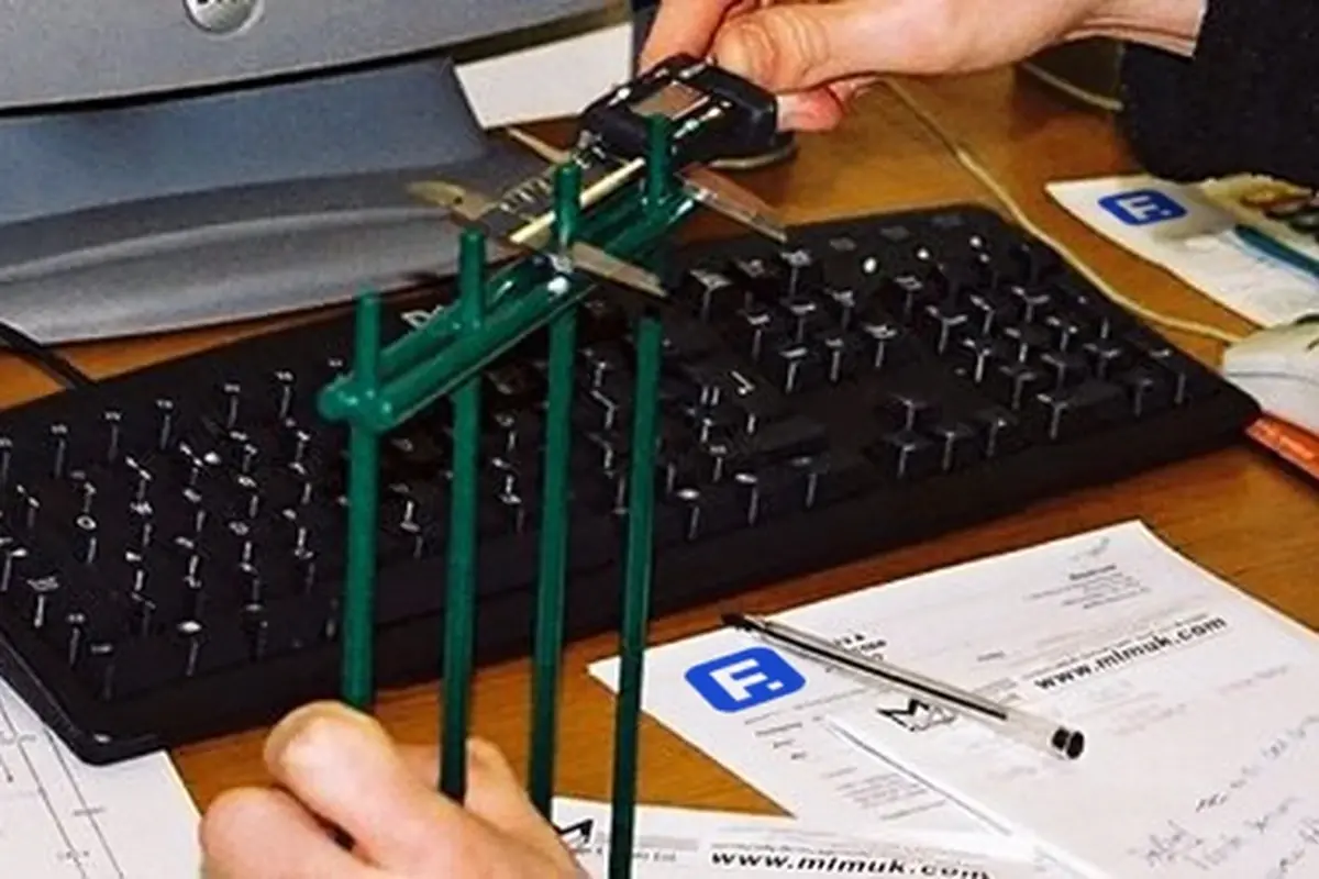 Hands handling a small physical fence sample beside review paperwork