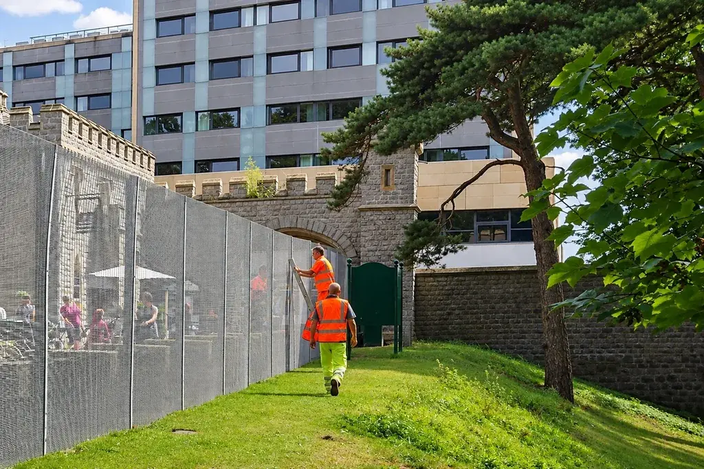 Workers installing mesh fencing beside changing ground levels