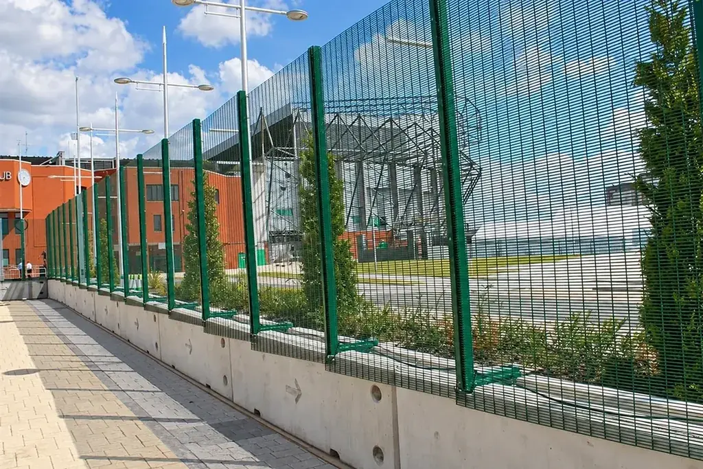 Installed green mesh fence running along a paved boundary