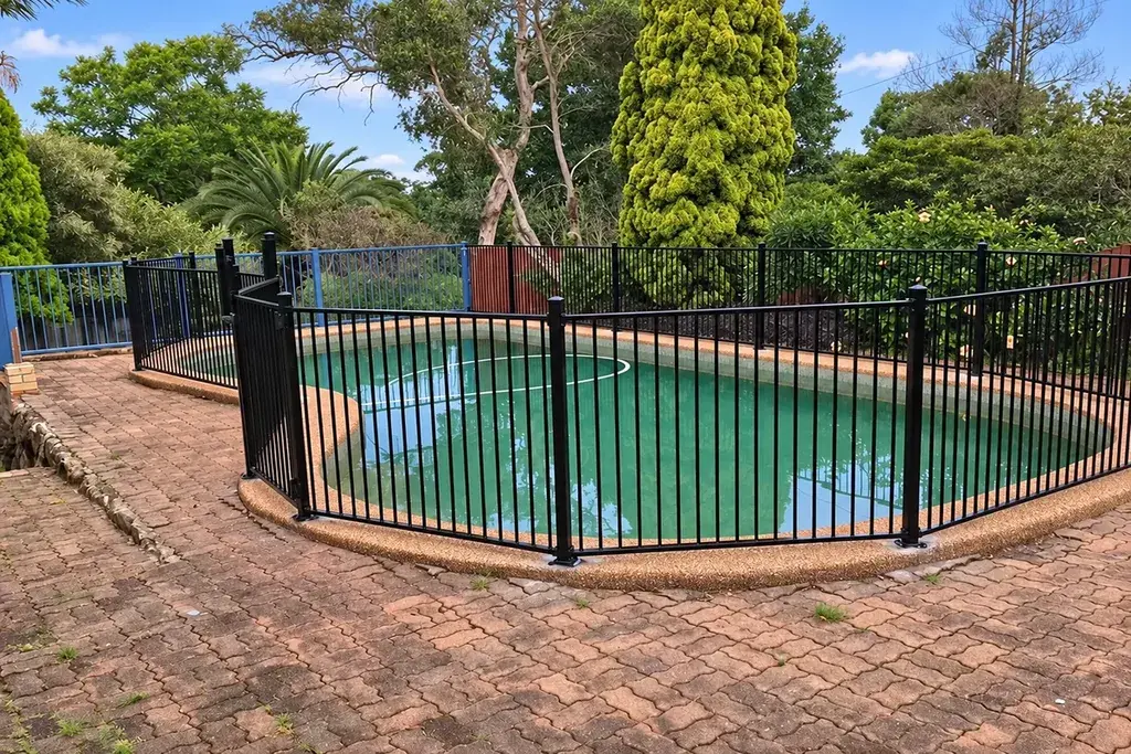 Black metal fence surrounding a backyard swimming pool