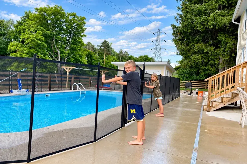 Person holding a gate at a fenced outdoor swimming pool