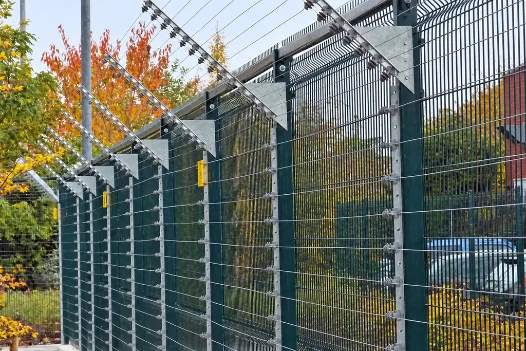 Electronic protection wires and brackets mounted above a security mesh fence