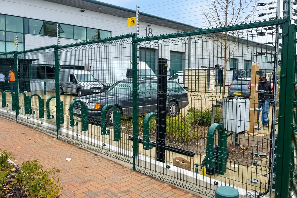 Electric fence wires above a green mesh fence at a vehicle entrance