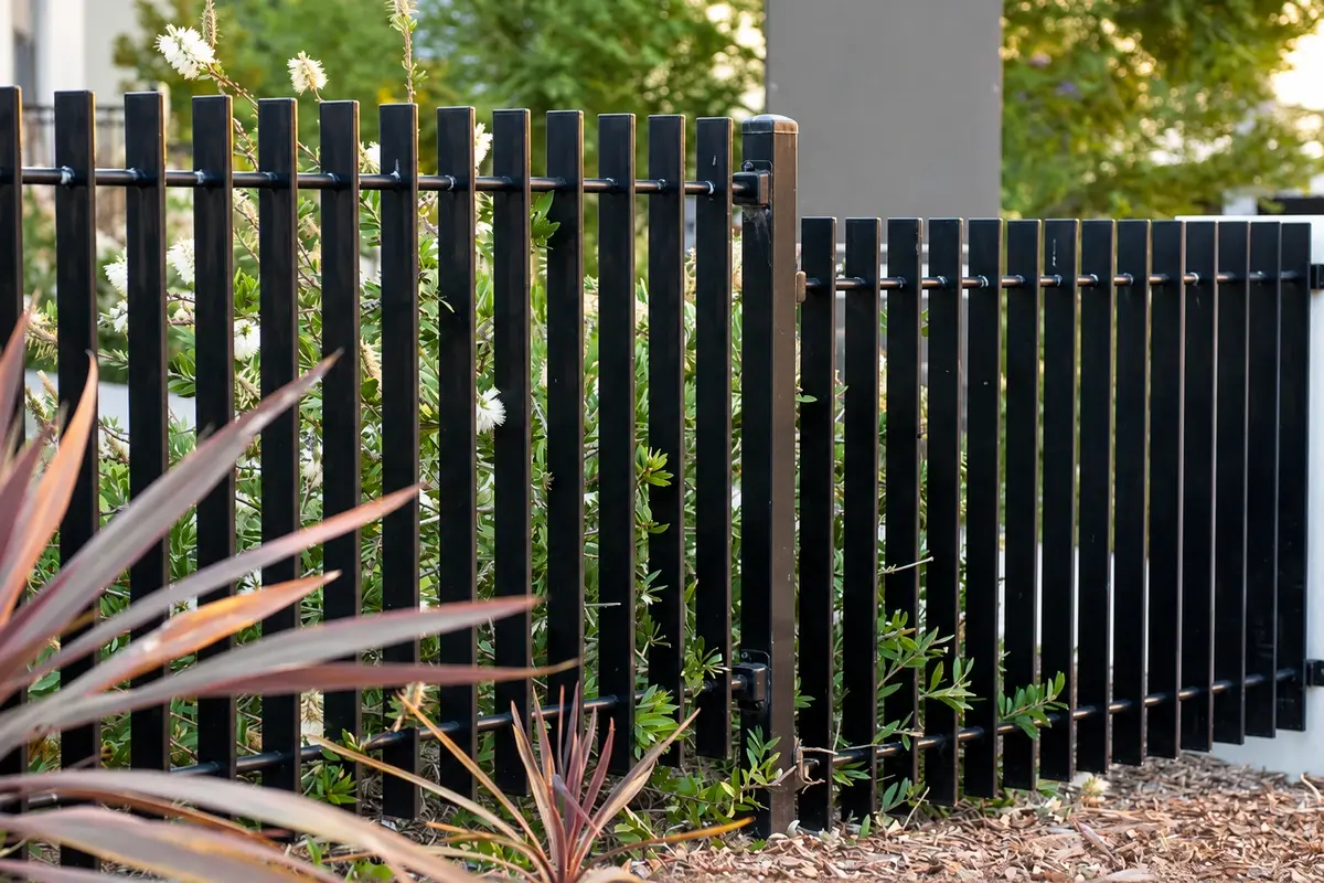 Black vertical metal privacy slats installed along a landscaped boundary