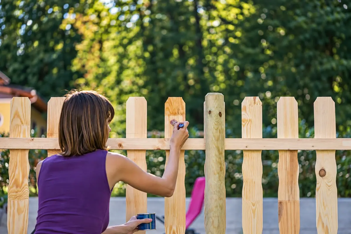 Person applying a maintenance coating to a timber picket fence