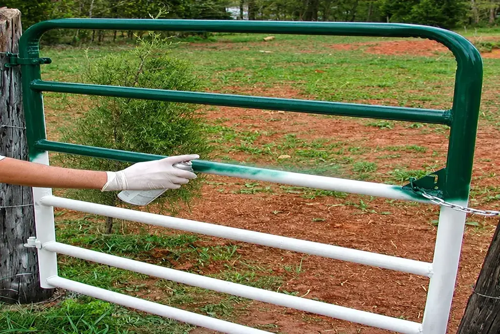 Person applying a protective coating to a metal farm gate during maintenance