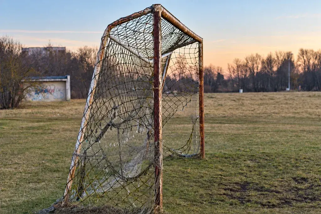 Heavily worn and distorted football goal frame and netting on a sports field