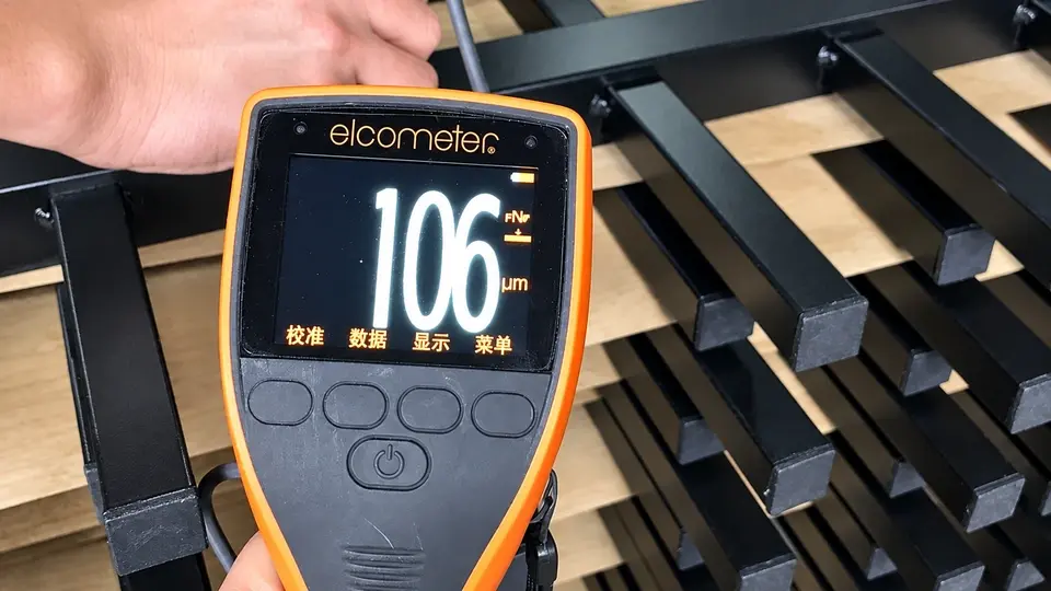 Handheld coating gauge checking a dark metal railing