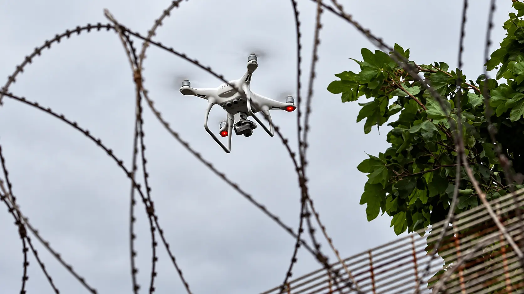Drone viewed through razor wire above a secure perimeter