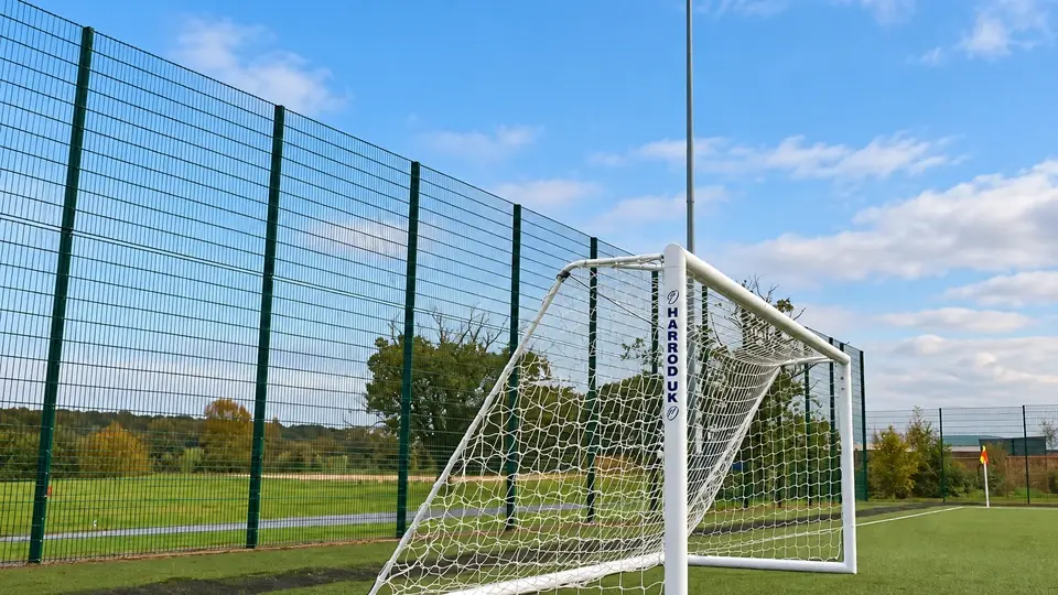 Football goal beside tall mesh fencing and floodlights