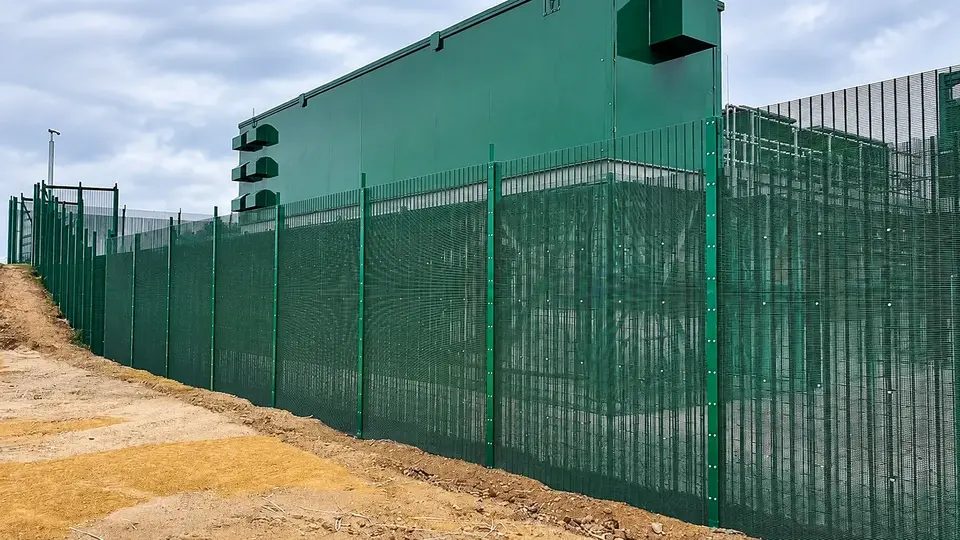 Green perimeter fence around a large industrial building