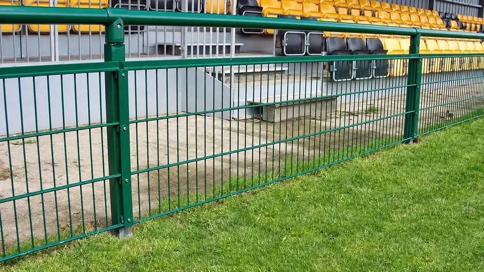 Low green spectator rail with mesh infill beside a pitch