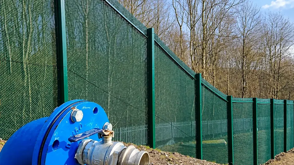 Mesh perimeter fence beside exposed utility pipework