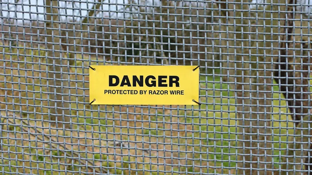 Razor wire warning sign attached to galvanized mesh fencing