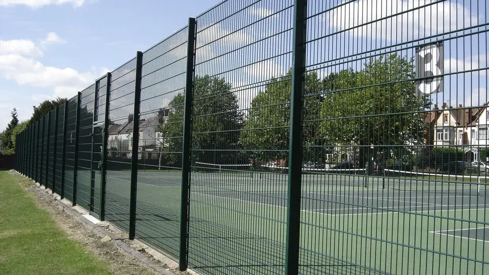 Outdoor mesh tennis court boundary beside grass and trees