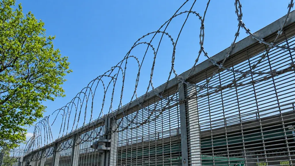Razor wire loops along the top of a metal perimeter fence