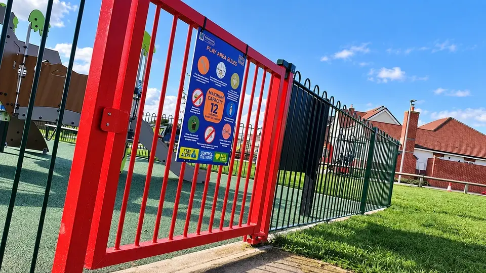 Red metal pedestrian gate at a playground entrance