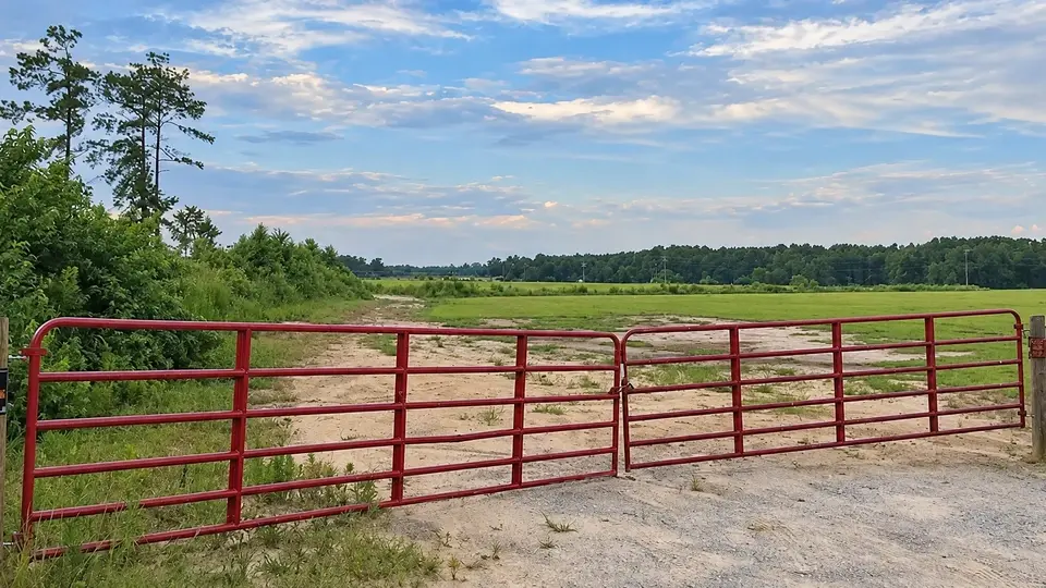 Red tubular double farm gates across a gravel driveway