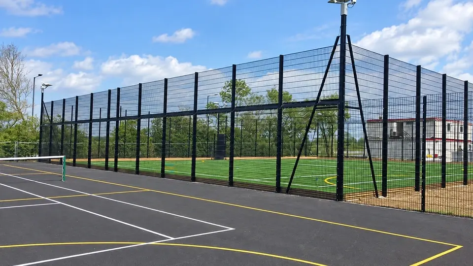 Floodlights mounted beside a tall school sports fence