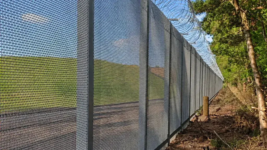 Tall mesh perimeter fence topped with razor wire