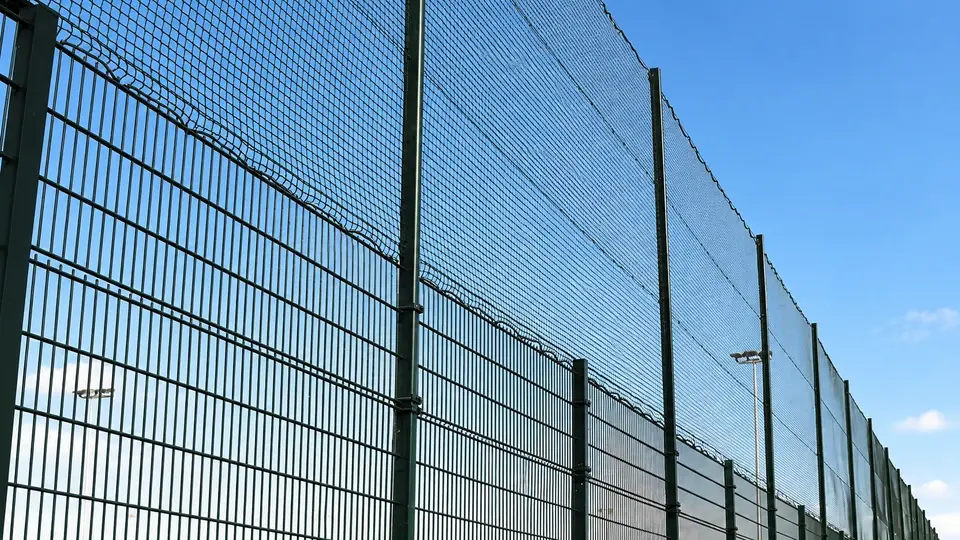 Tall green mesh fencing above a lower sports boundary fence