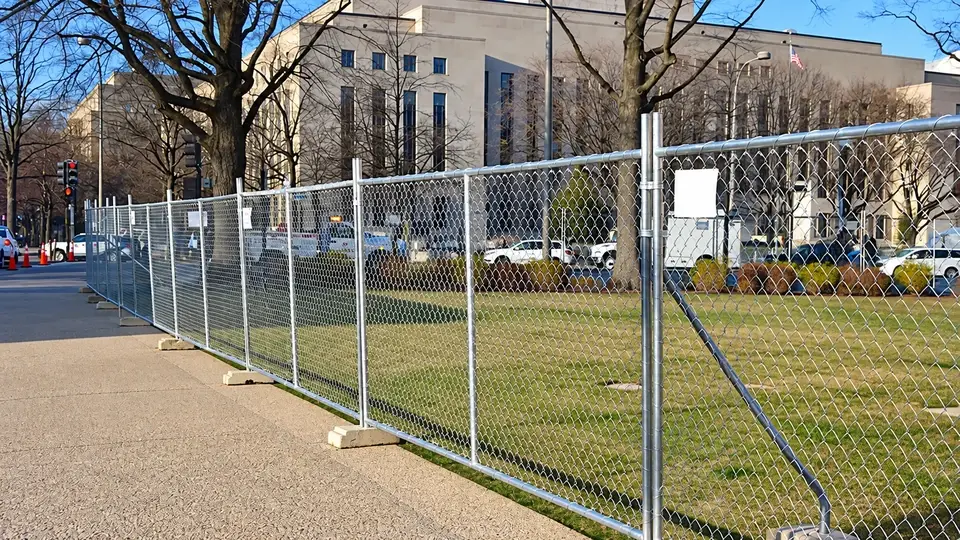 Temporary chain link fence on concrete feet beside a pavement