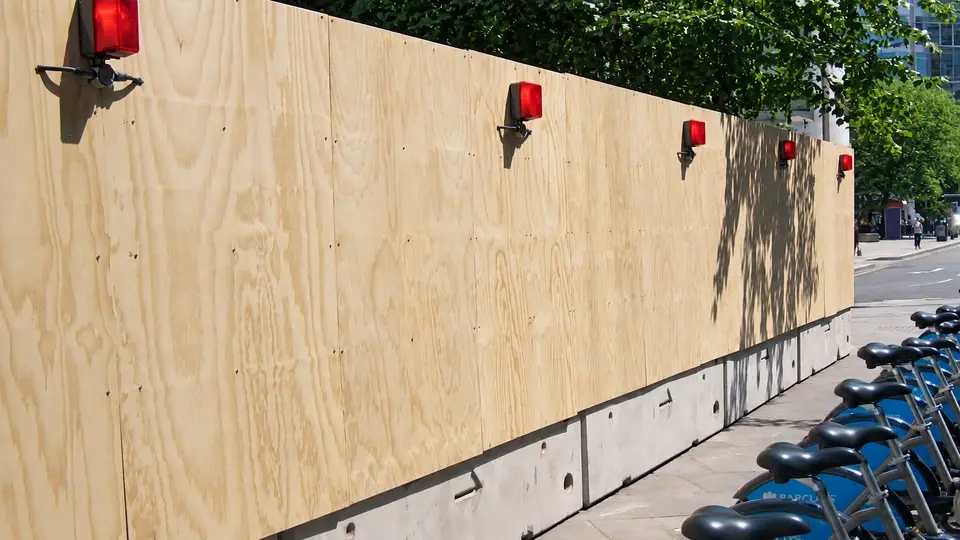 Solid timber construction hoarding with red lights beside a pavement