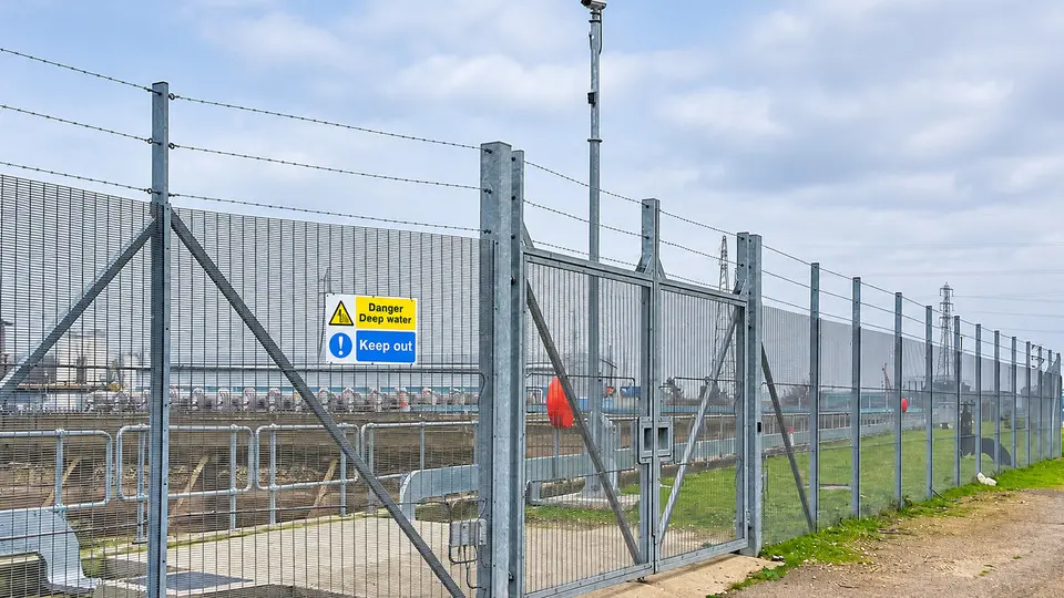 A camera mast above mesh gates at a utility site