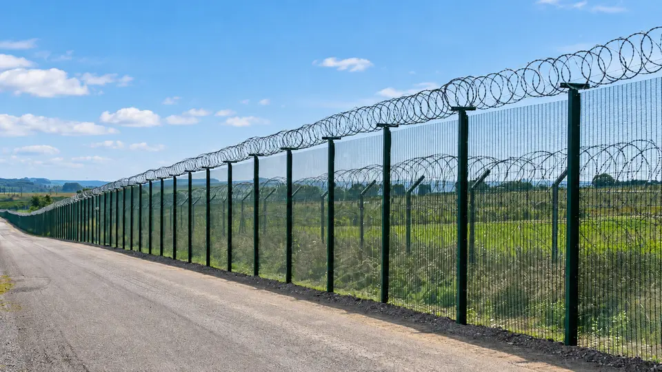 Green security fence following a long sloping roadside