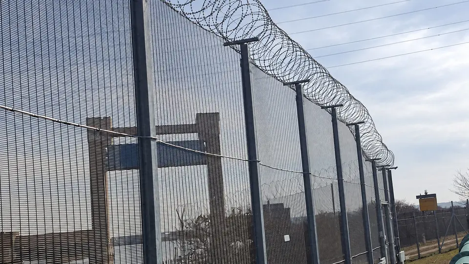 Coiled razor wire supported above a tall security mesh fence