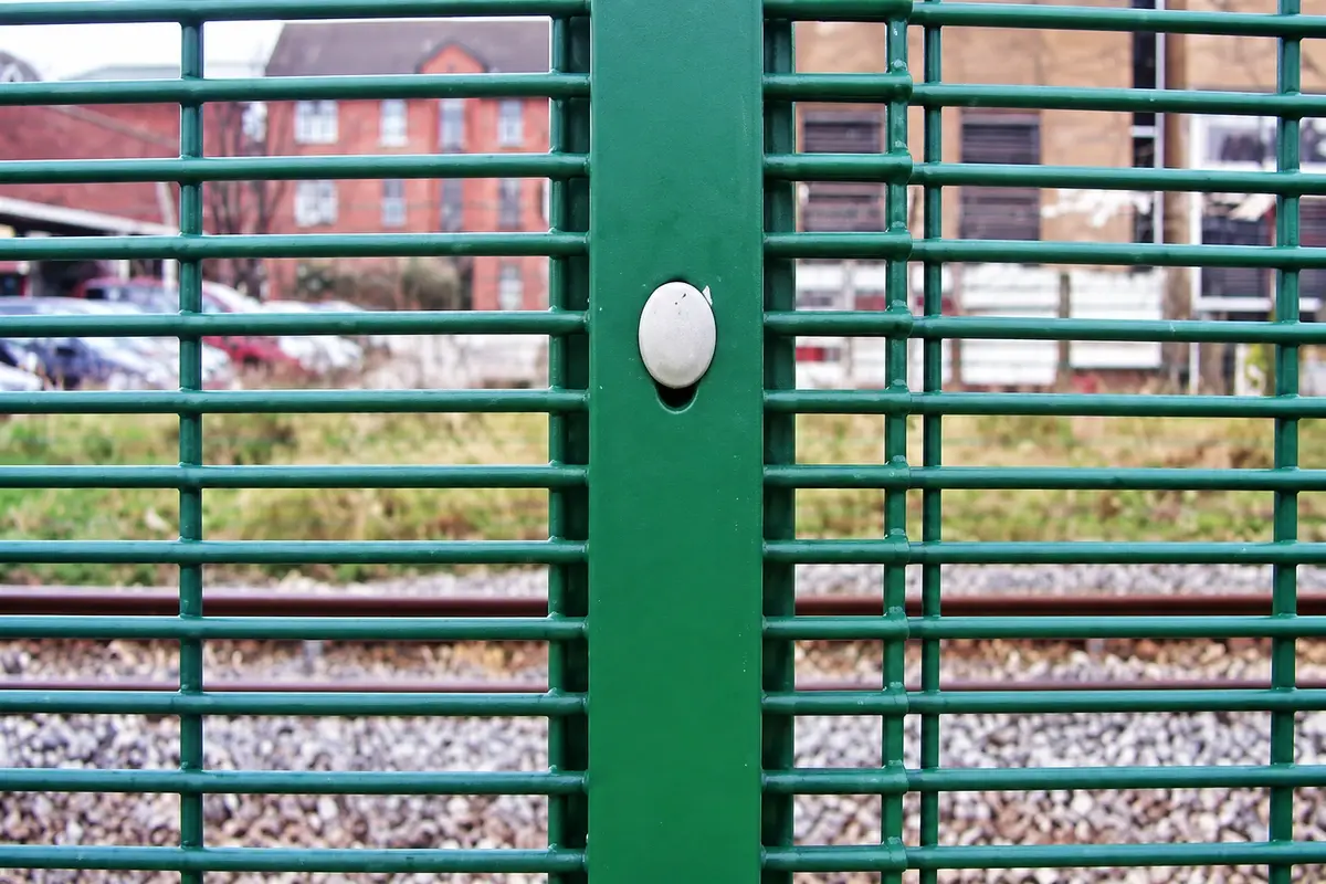 Green clamp bar and bolt securing horizontal mesh wires at a post