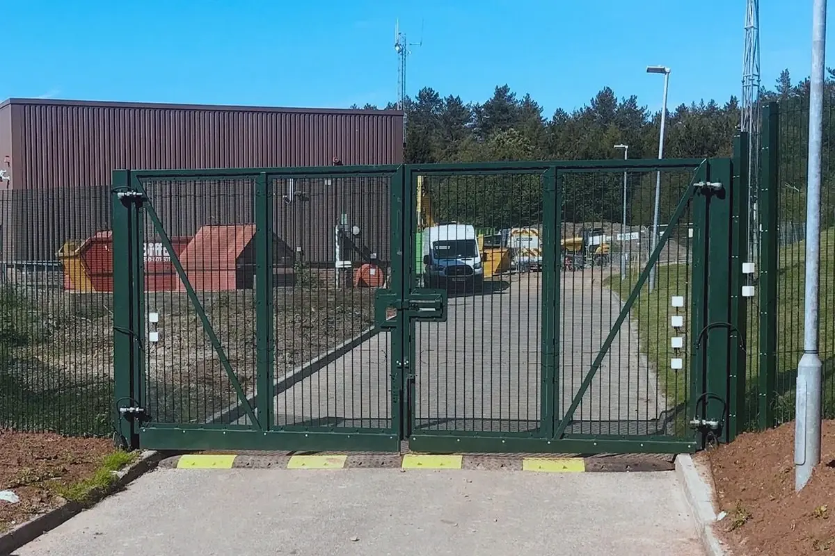 Green close-mesh vehicle gate with framed leaves and hinge posts