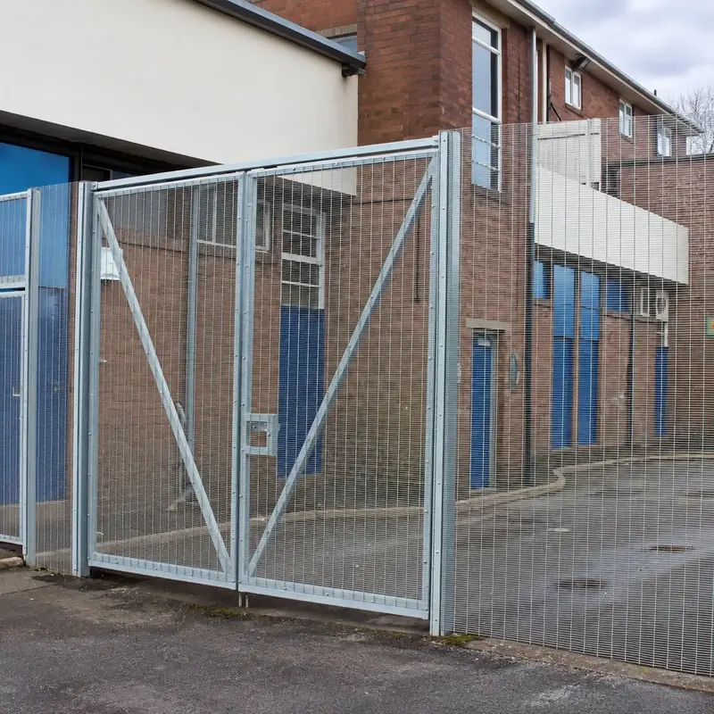 Silver close-mesh double-leaf vehicle gate at a building entrance