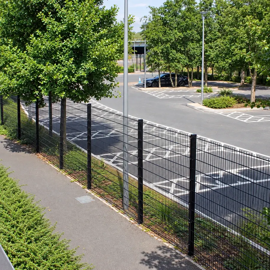 Black double-wire fence separating a footpath and car park