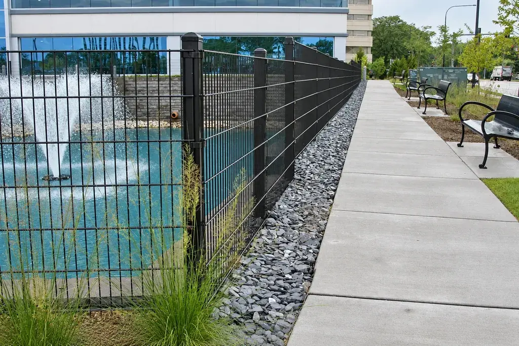 Black welded mesh fencing and posts beside a paved walkway