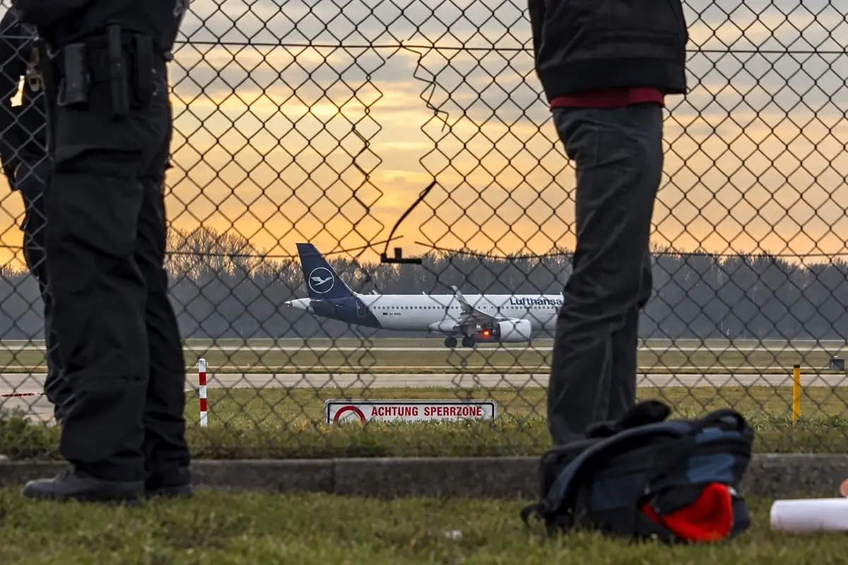 People beside a chain link airport fence with an aircraft beyond