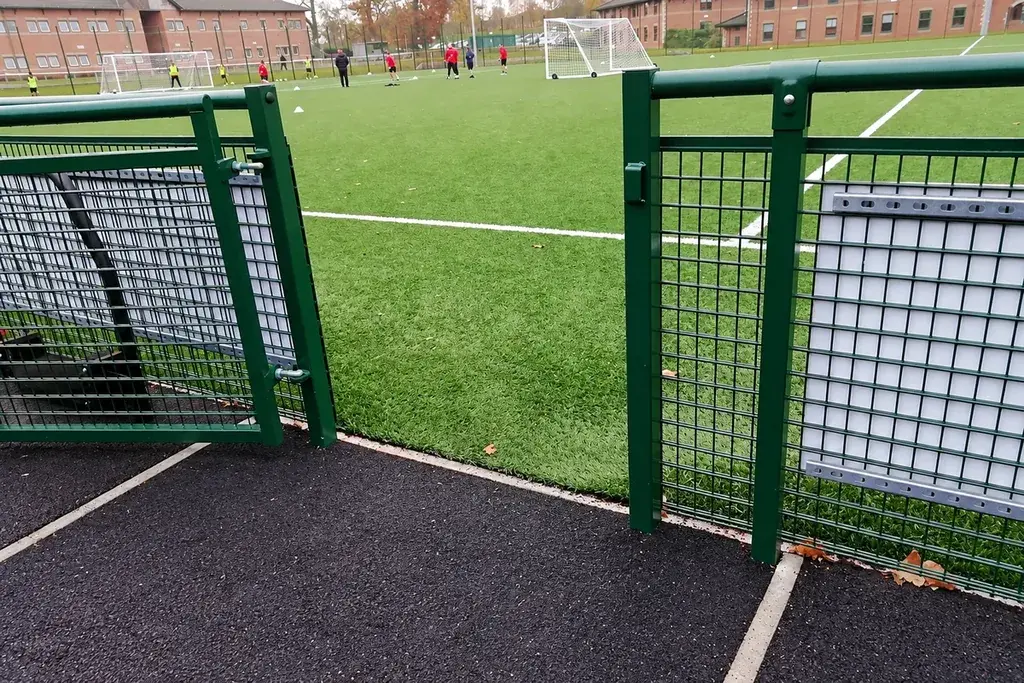 Sports enclosure access gate and adjoining mesh fence
